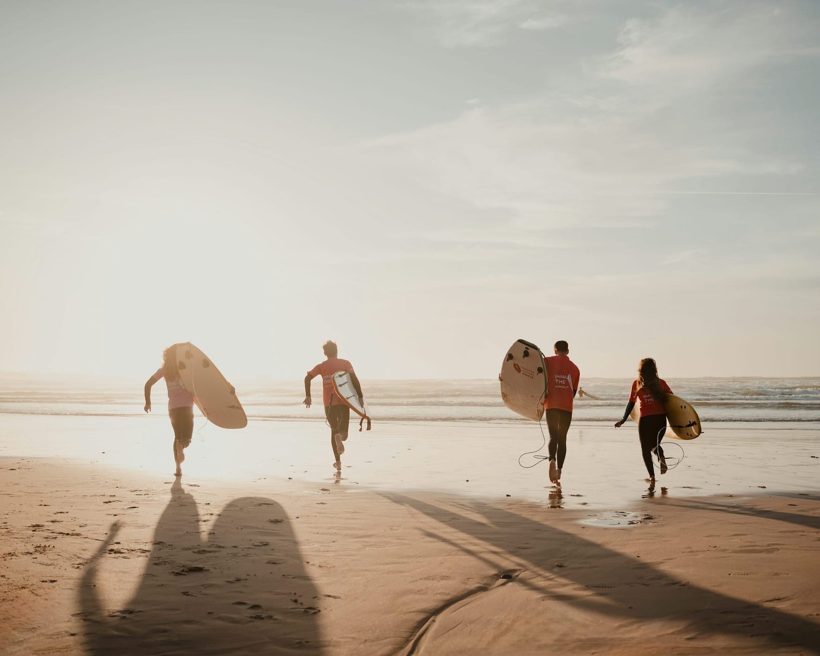 Four surfers running into the Atlantic with their boards under golden morning light in Taghazout